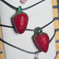 Strawberry and blackberry charms on a string with a white background